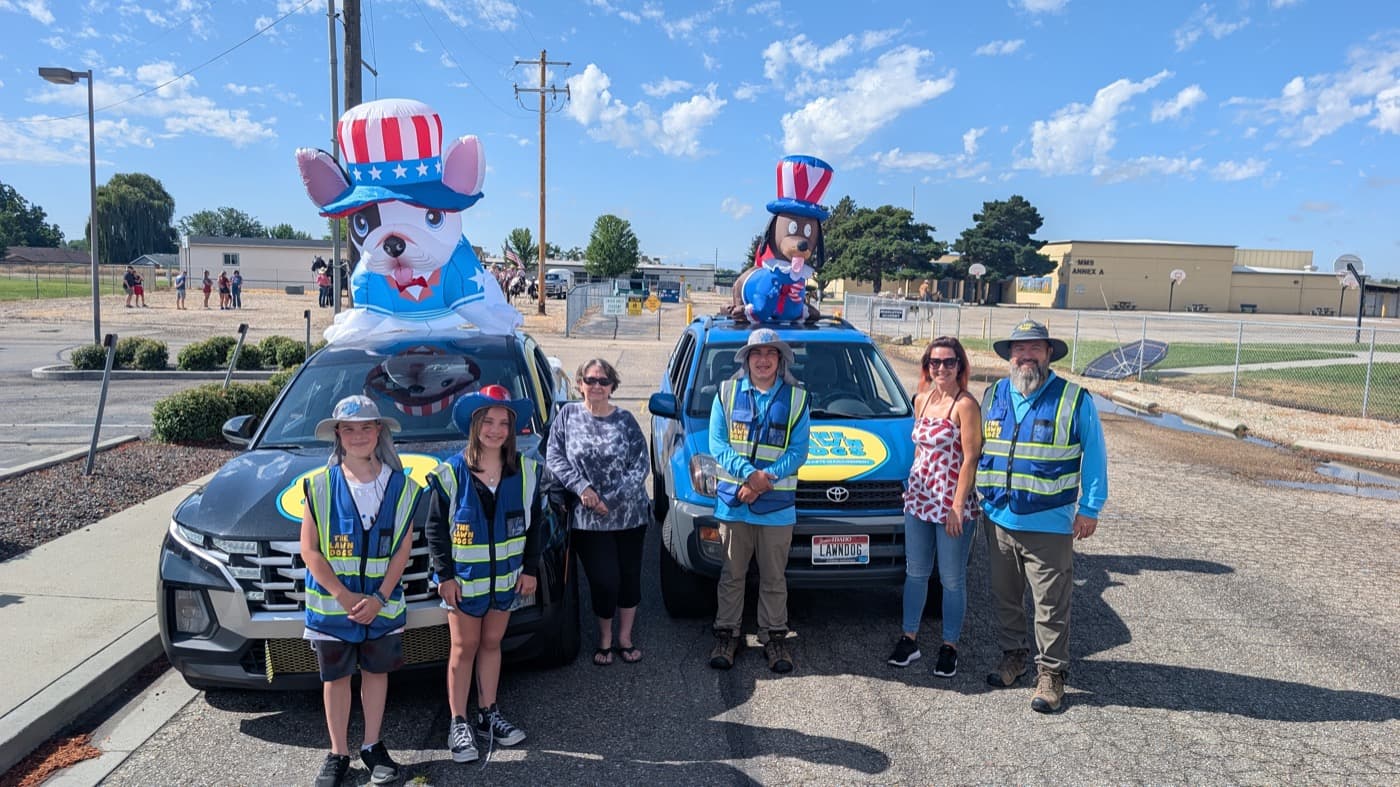 The Lawn Dogs team in branded vests beside two decorated company trucks with inflatable dogs, staged for the Middleton parade